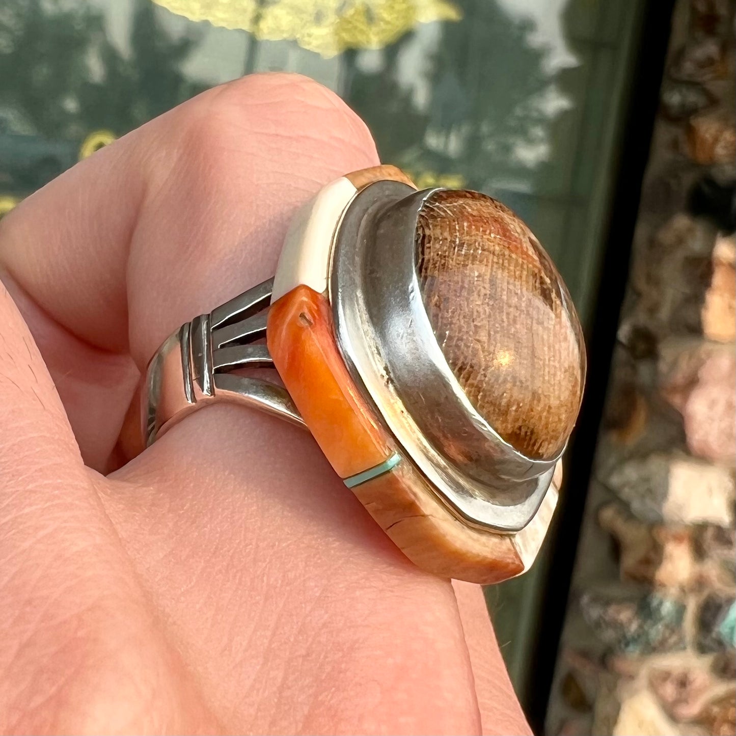 A silver ring handmade from a bezel set petrified wood stone, surrounded by quartz, carnelian, and bone inlay.