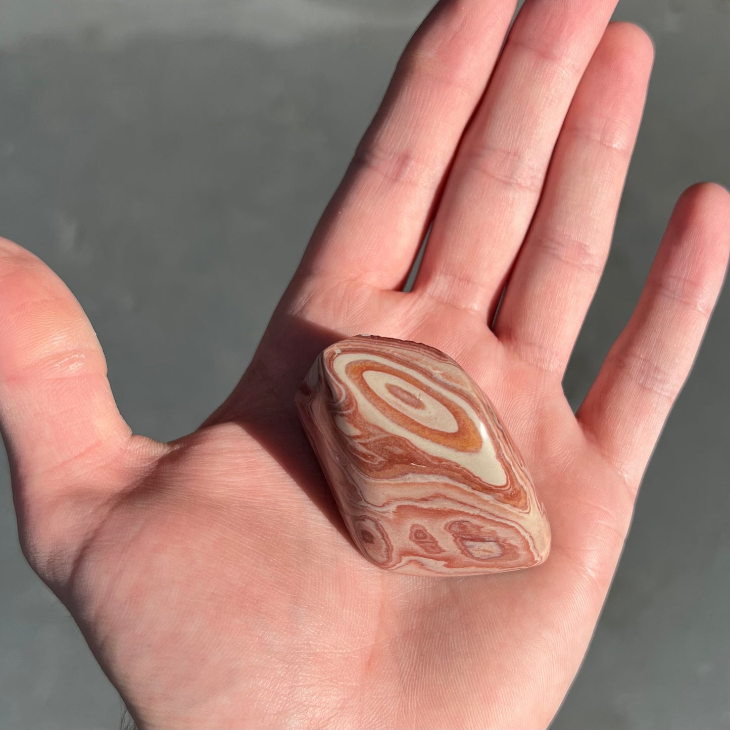 A polished piece of pinkish red picture jasper.  The stone displays a bull's eye pattern.