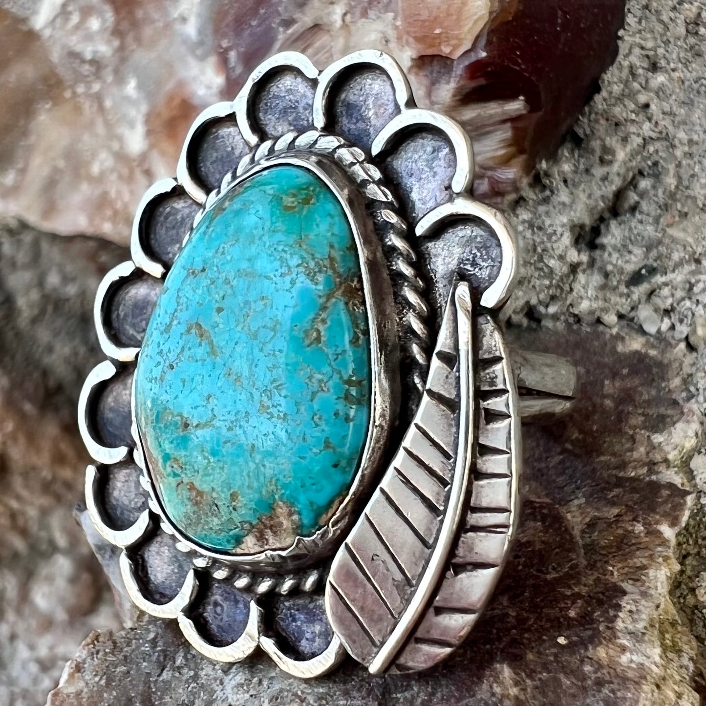 A sterling silver Navajo style ring.  The ring is set with a turquoise stone from Pilot Mountain.  There is a feather decoration next to the stone.