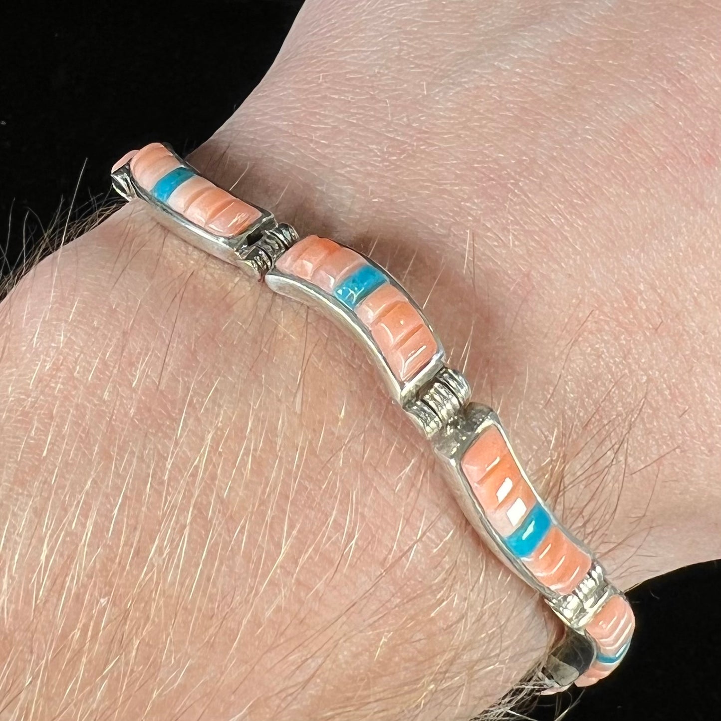 A ladies' sterling silver tennis style bracelet set with polished pink coral and turquoise inlay.