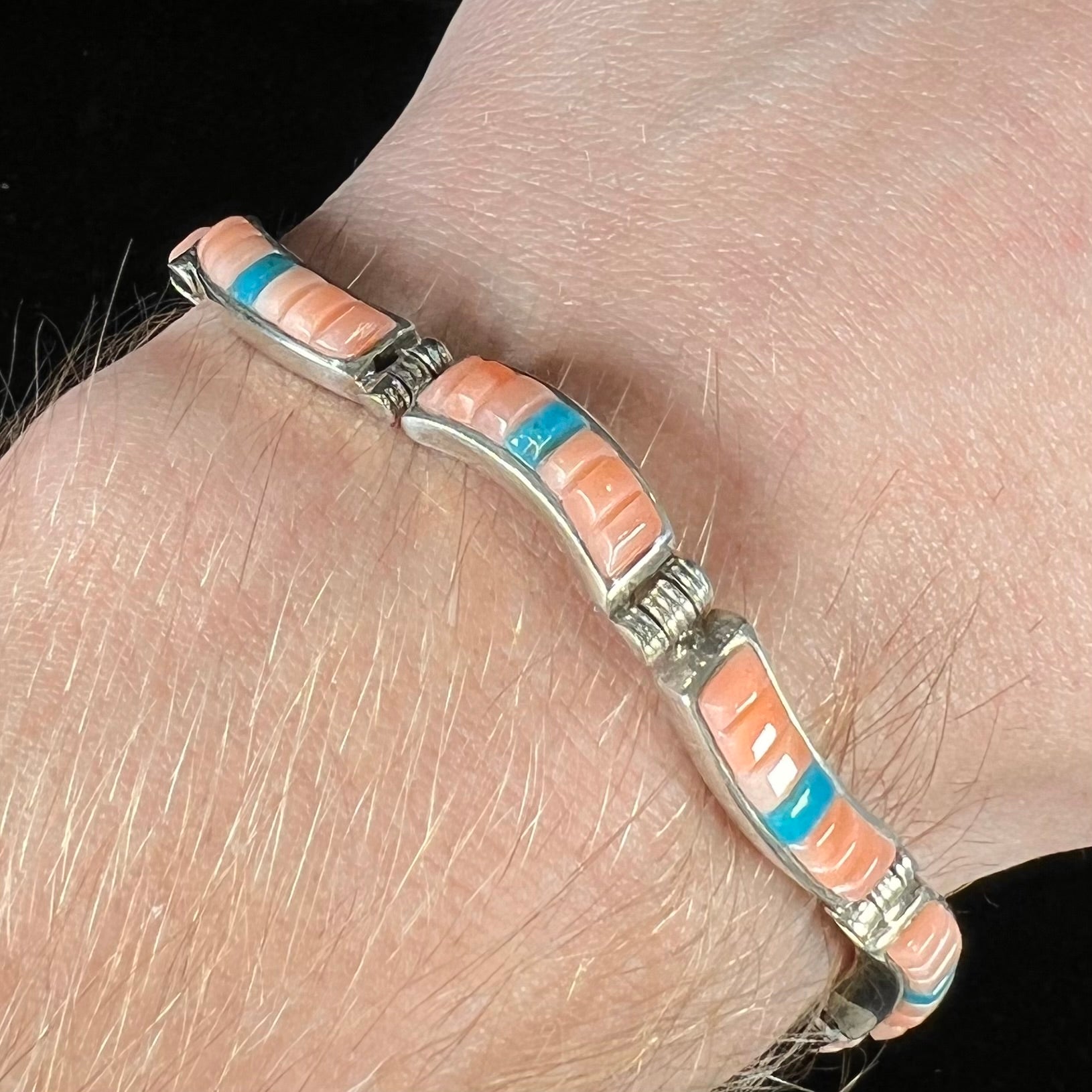 A ladies' sterling silver tennis style bracelet set with polished pink coral and turquoise inlay.