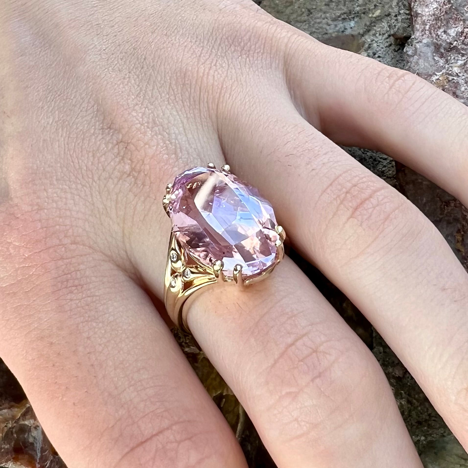 A large, pink kunzite is prong set into a 14kt yellow gold basket-style ring mounting with three diamonds flush set into the design on each side.