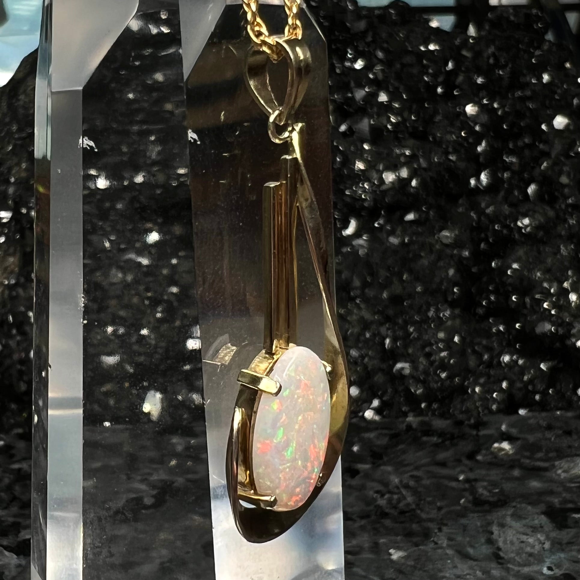 A handmade gold drop pendant set with an oval cabochon cut white crystal opal.