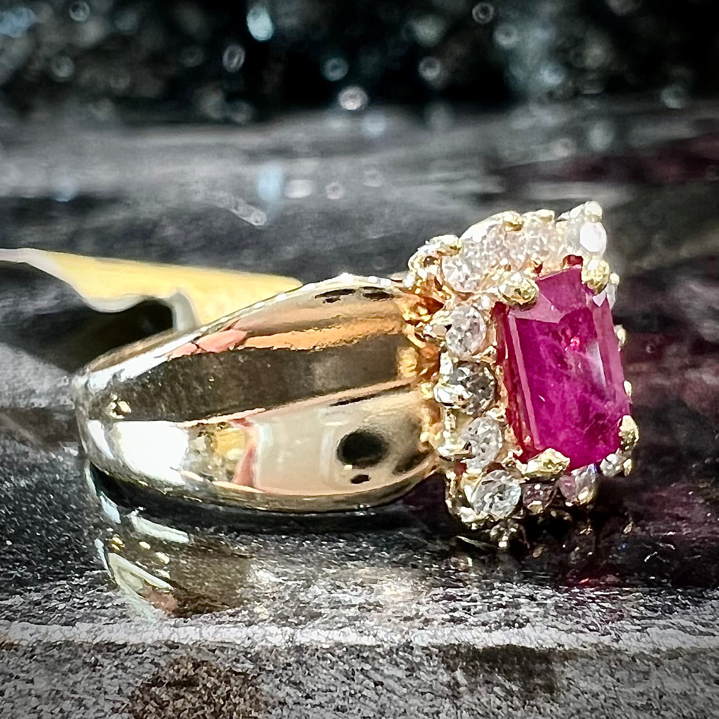 A yellow gold ring set with an emerald cut red ruby surrounded by a halo of round diamonds.