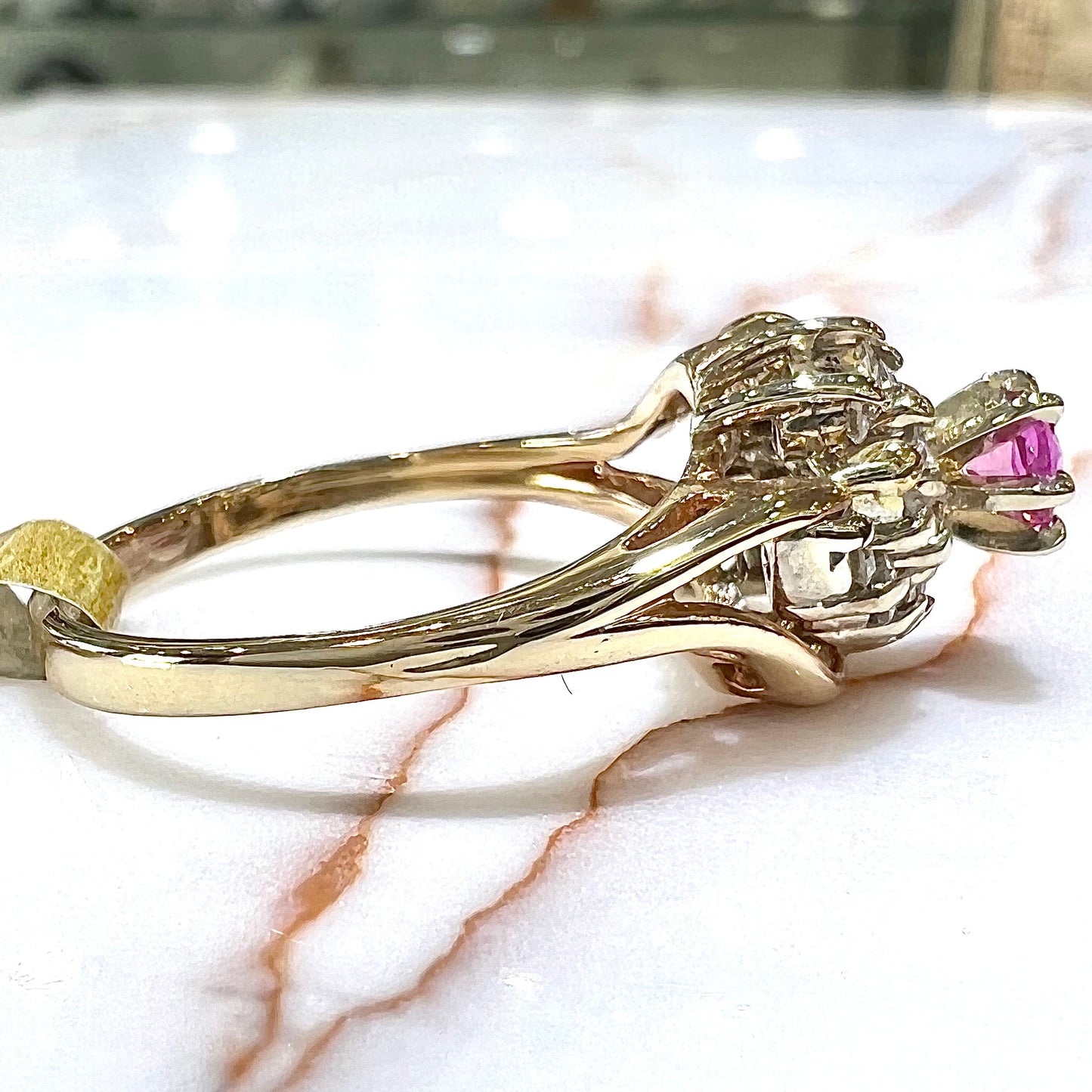 A round pink sapphire high-set in a yellow gold diamond cluster ring.