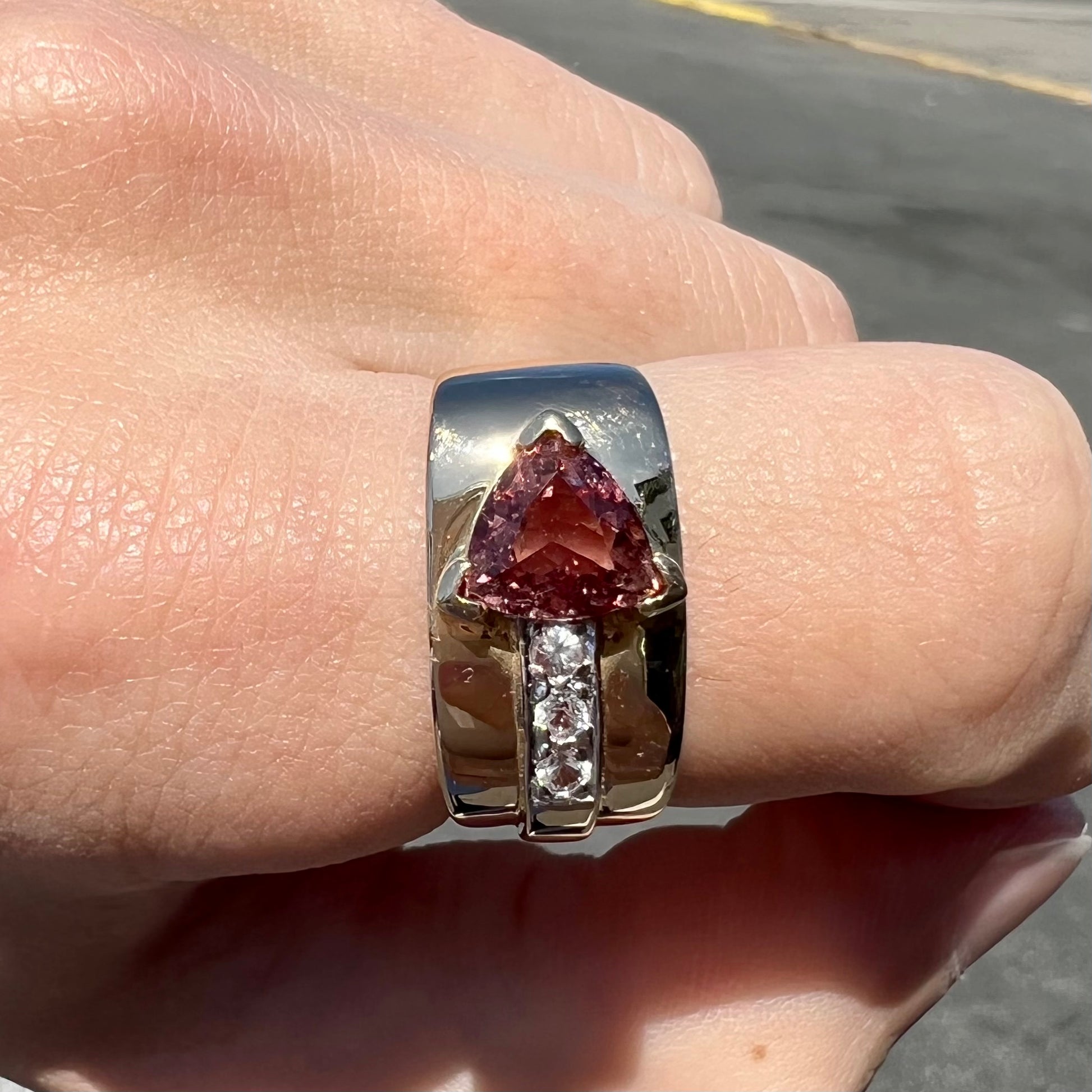 A men's gold pink tourmaline ring.  Set next to the trillion cut tourmaline is a row of three round white sapphires.