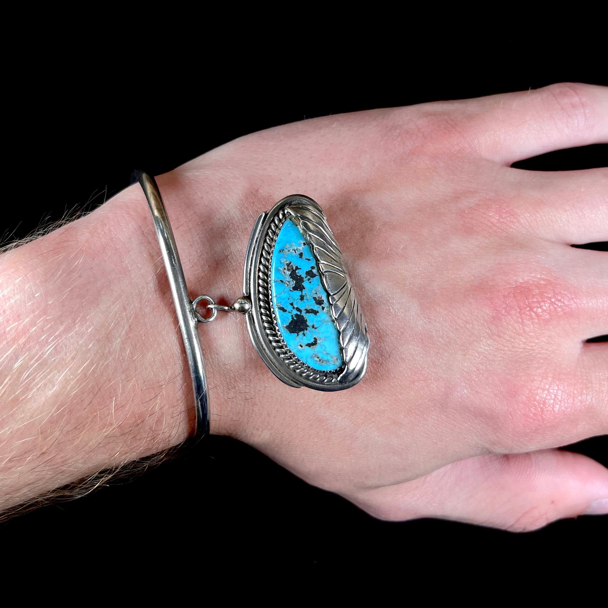 A sterling silver cuff bracelet with an attached dangle segment set with a turquoise stone from Pinto Valley.