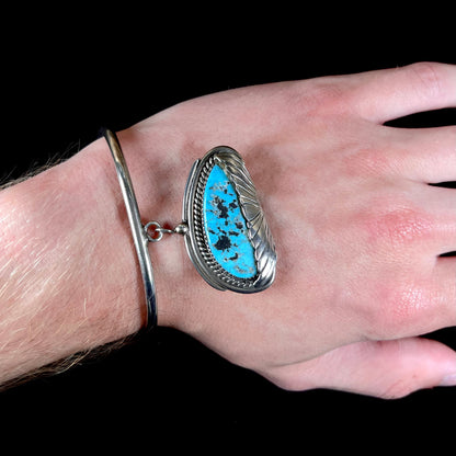 A sterling silver cuff bracelet with an attached dangle segment set with a turquoise stone from Pinto Valley.