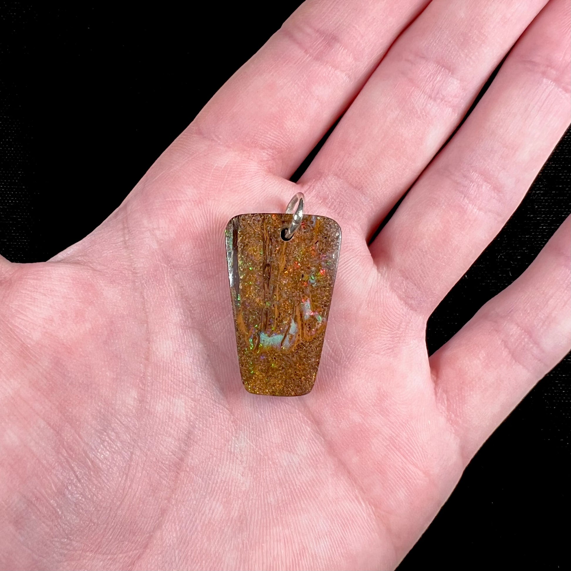 A drilled boulder opal stone with a sterling silver ring through the hole to be worn as a pendant.
