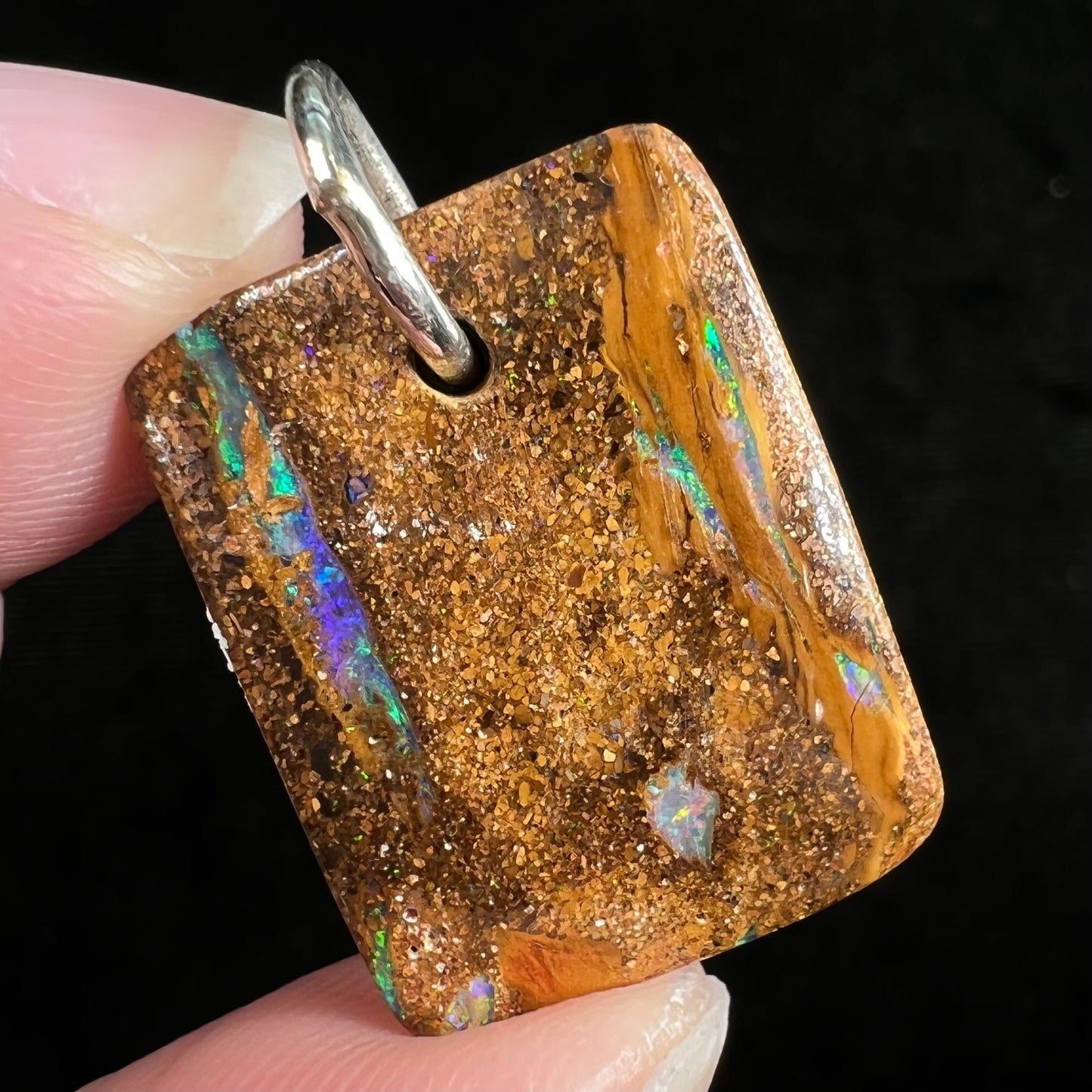 A drilled boulder opal stone with a sterling silver ring through the hole to be worn as a pendant.