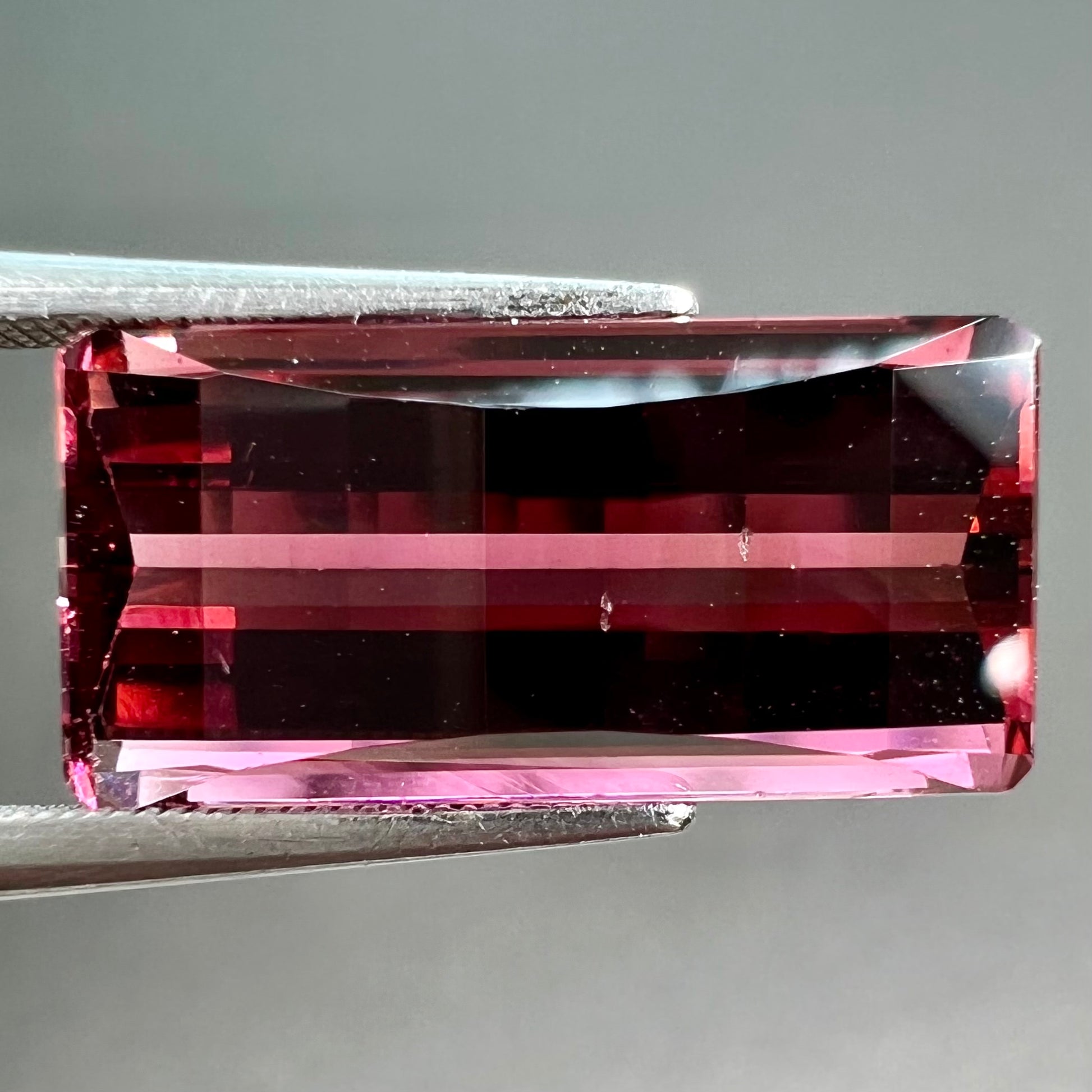 A loose, fantasy cut reddish colored tourmaline.  The cut reflects light in a way that resembles digital pixels on a screen.