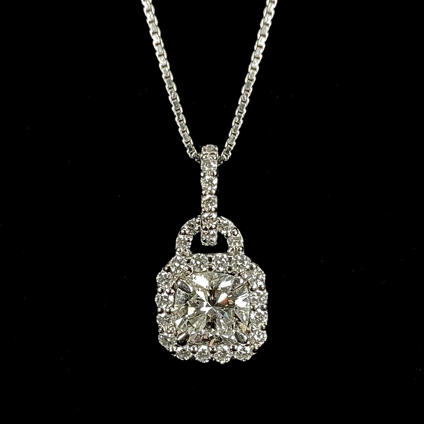 A ladies' platinum diamond halo necklace set with a 0.58ct cushion cut diamond on a box chain.