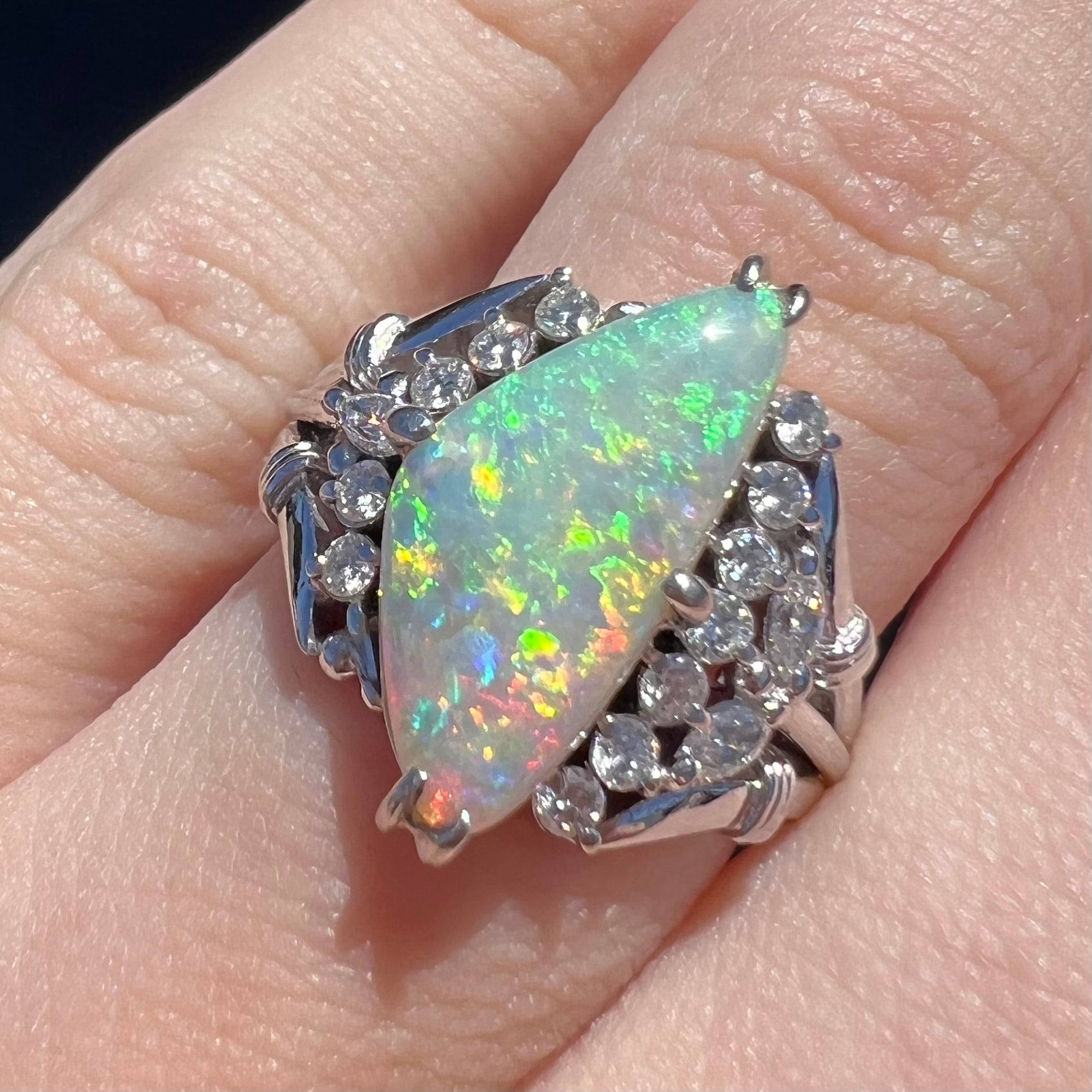 A freeform triangular cabochon cut Lightning Ridge white crystal opal set with diamonds in an ornate platinum split shank setting.