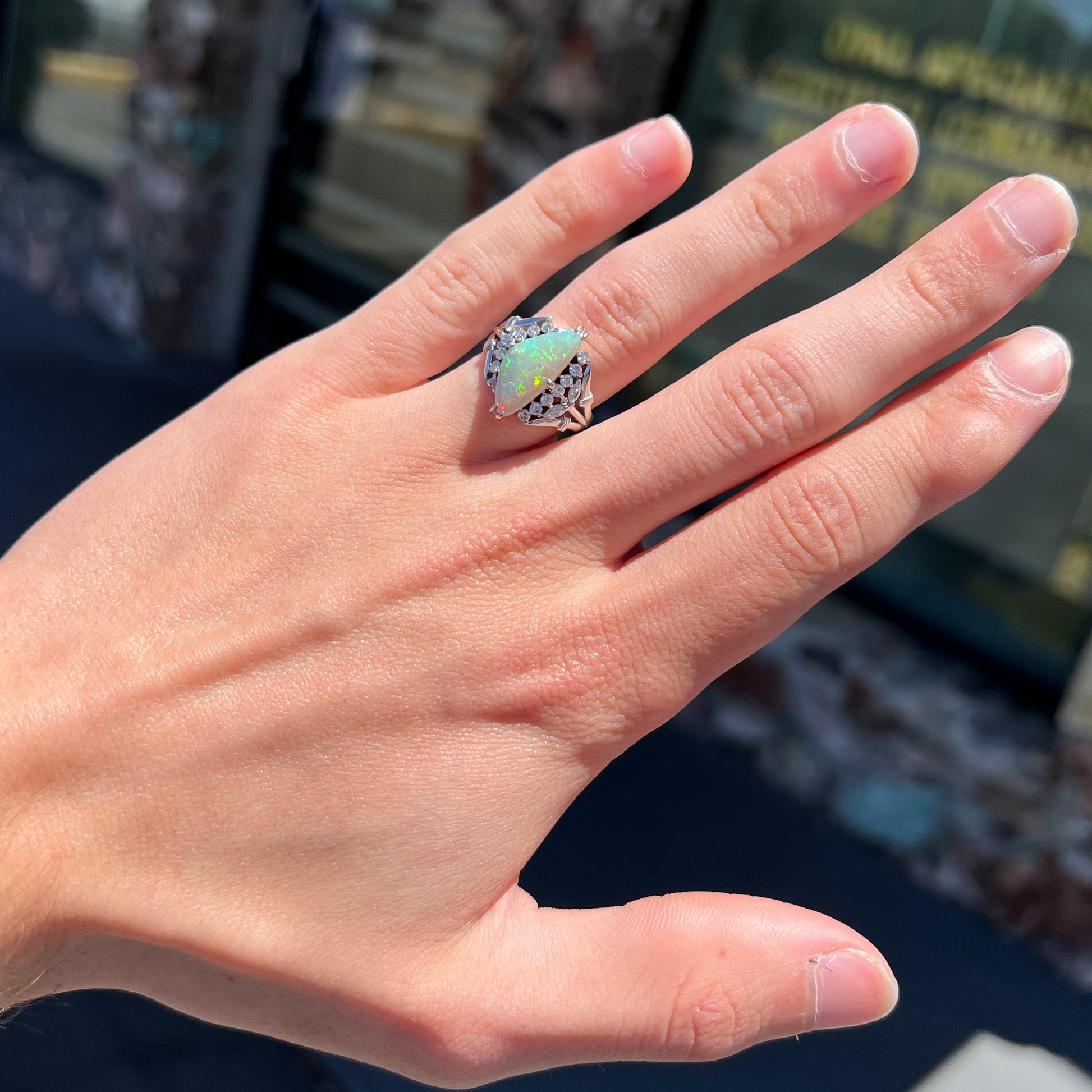 A freeform triangular cabochon cut Lightning Ridge white crystal opal set with diamonds in an ornate platinum split shank setting.