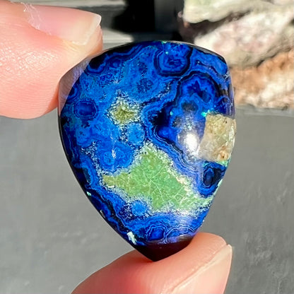 A loose pear shape cabochon cut blue azurite stone with green pseudomalachite inclusions.