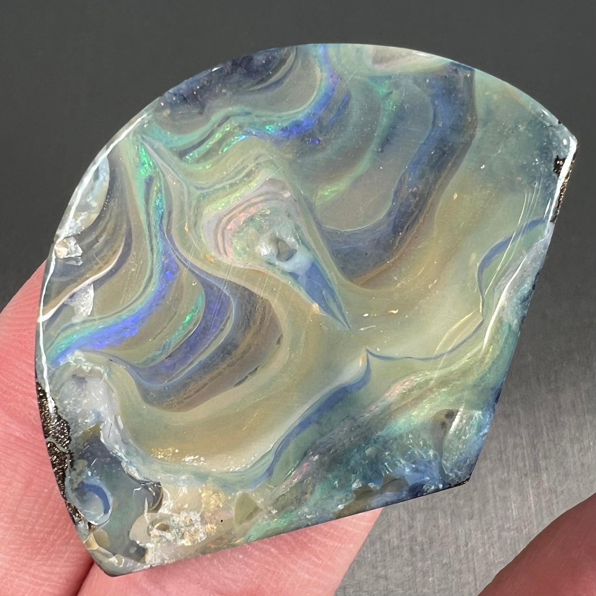 A polished, loose boulder opal stone from Queensland, Australia.  Fire colors are green, blue, purple, and salmon.