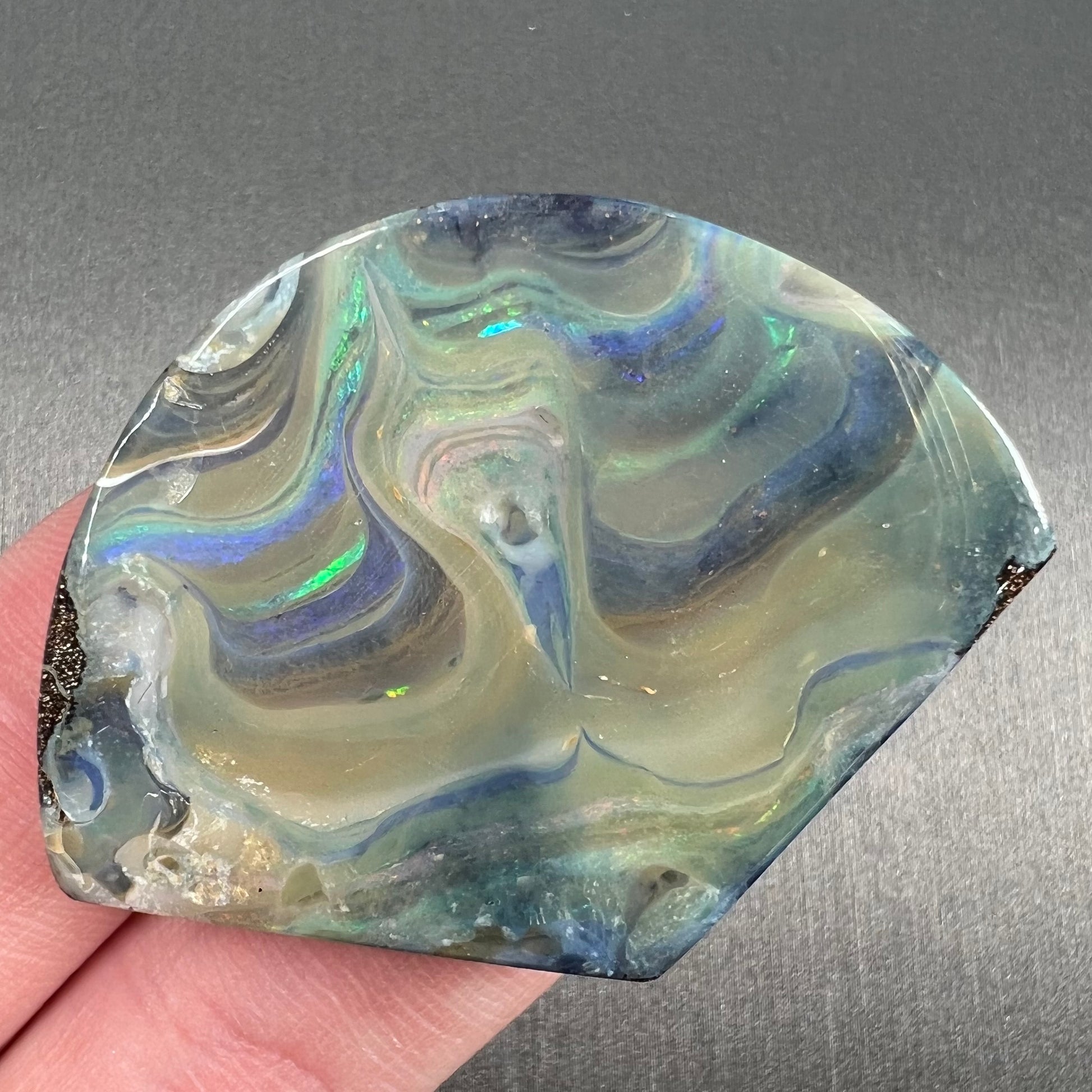 A polished, loose boulder opal stone from Queensland, Australia.  Fire colors are green, blue, purple, and salmon.