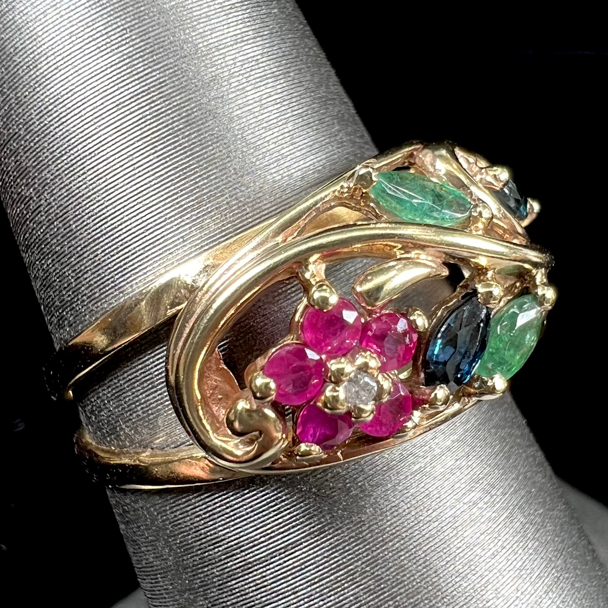 A yellow gold ladies' ring featuring the motif of a flower with leaves set with emeralds, rubies, sapphires, and a  diamond.