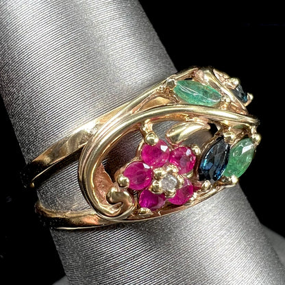 A yellow gold ladies' ring featuring the motif of a flower with leaves set with emeralds, rubies, sapphires, and a  diamond.