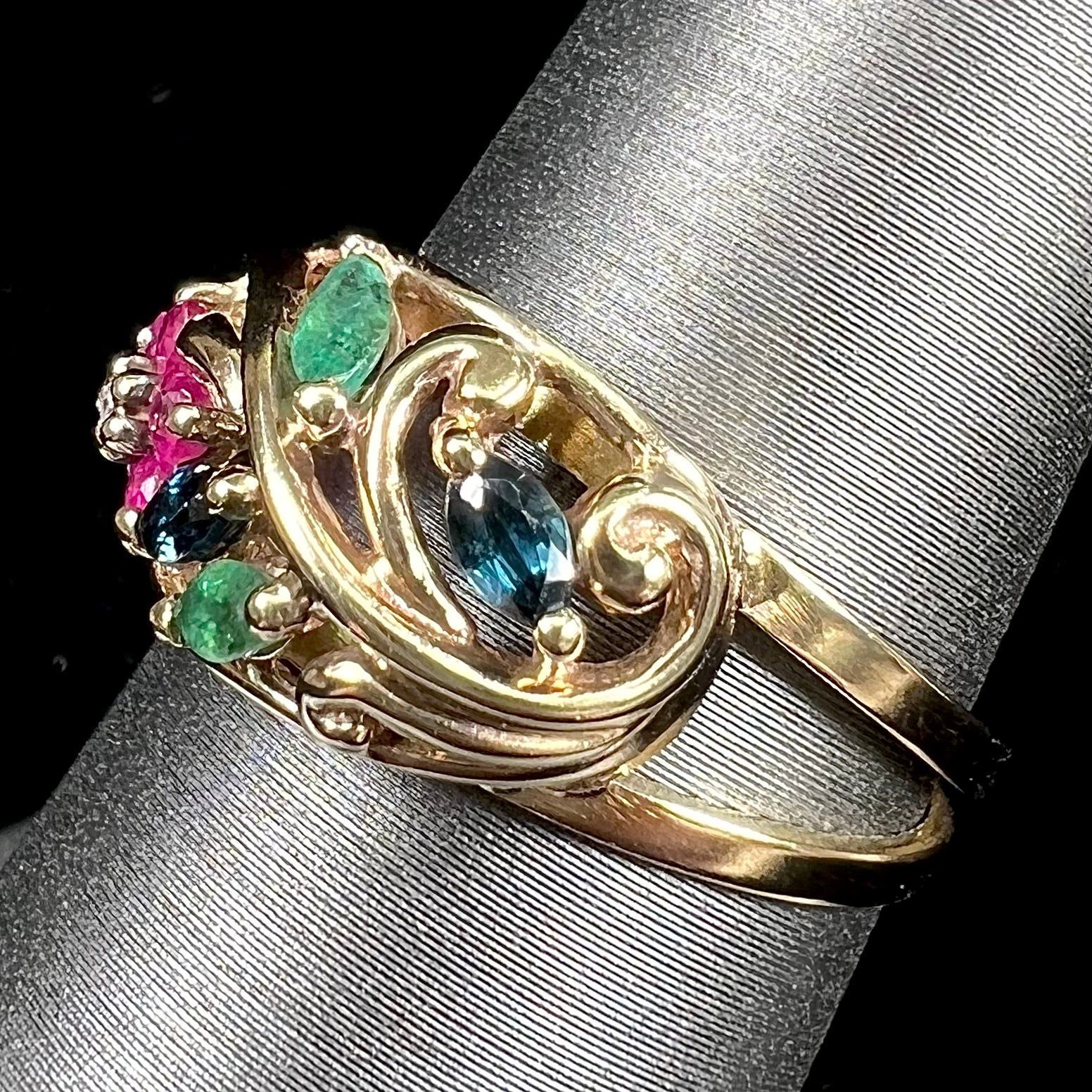 A yellow gold ladies' ring featuring the motif of a flower with leaves set with emeralds, rubies, sapphires, and a  diamond.
