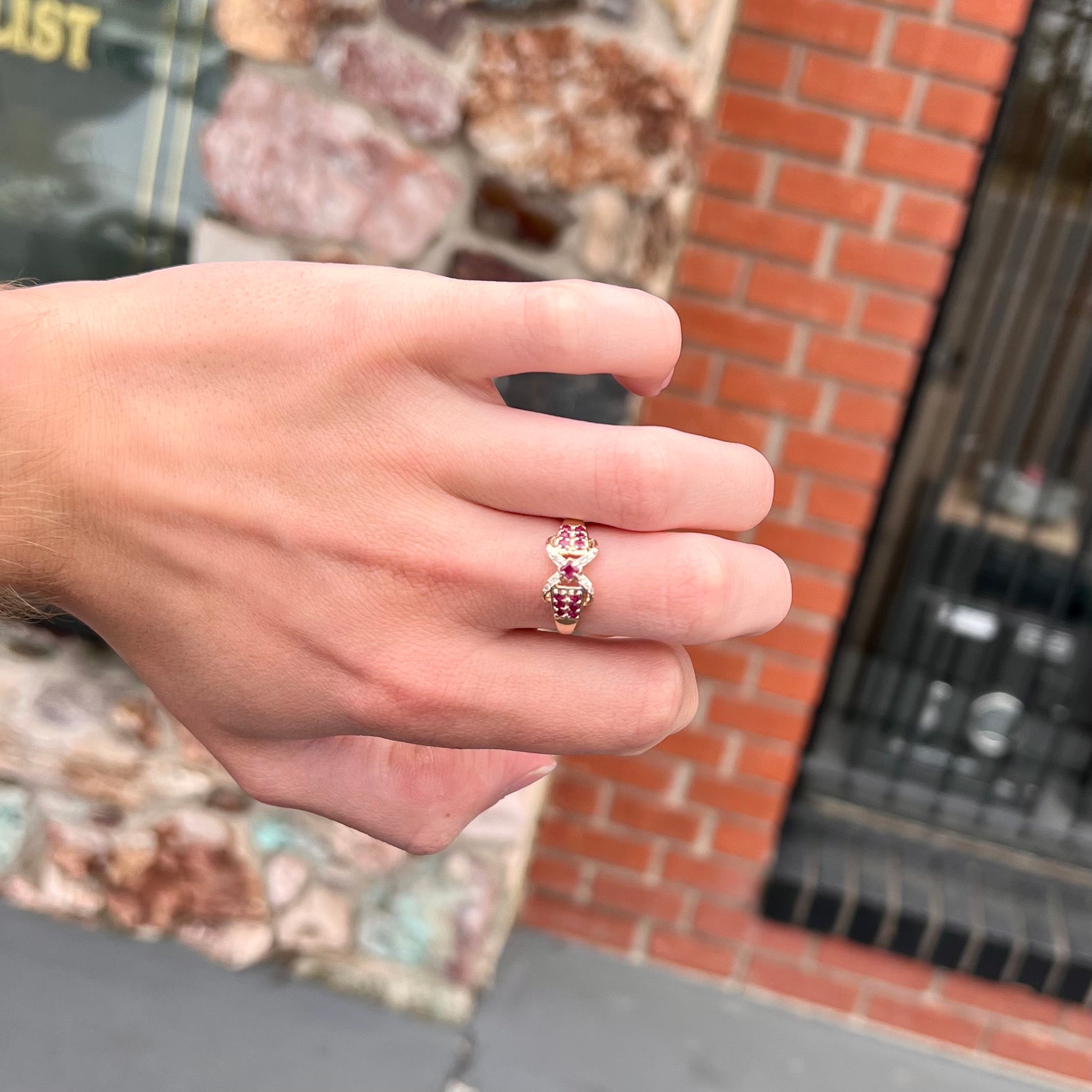 A yellow gold princess cut ruby ring set with round ruby and diamond accents.