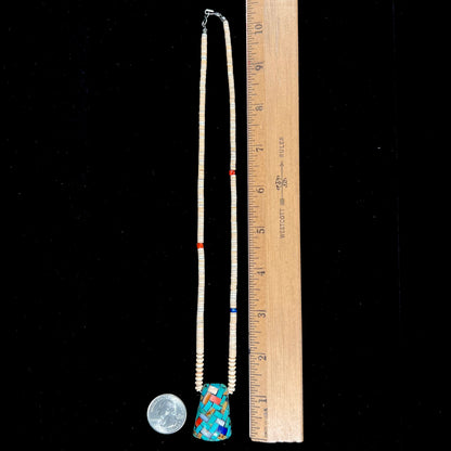 A three dimensional mosaic stone inlay pendant set with turquoise, lapis lazuli, coral, and mother of pearl on a puka shell necklace.