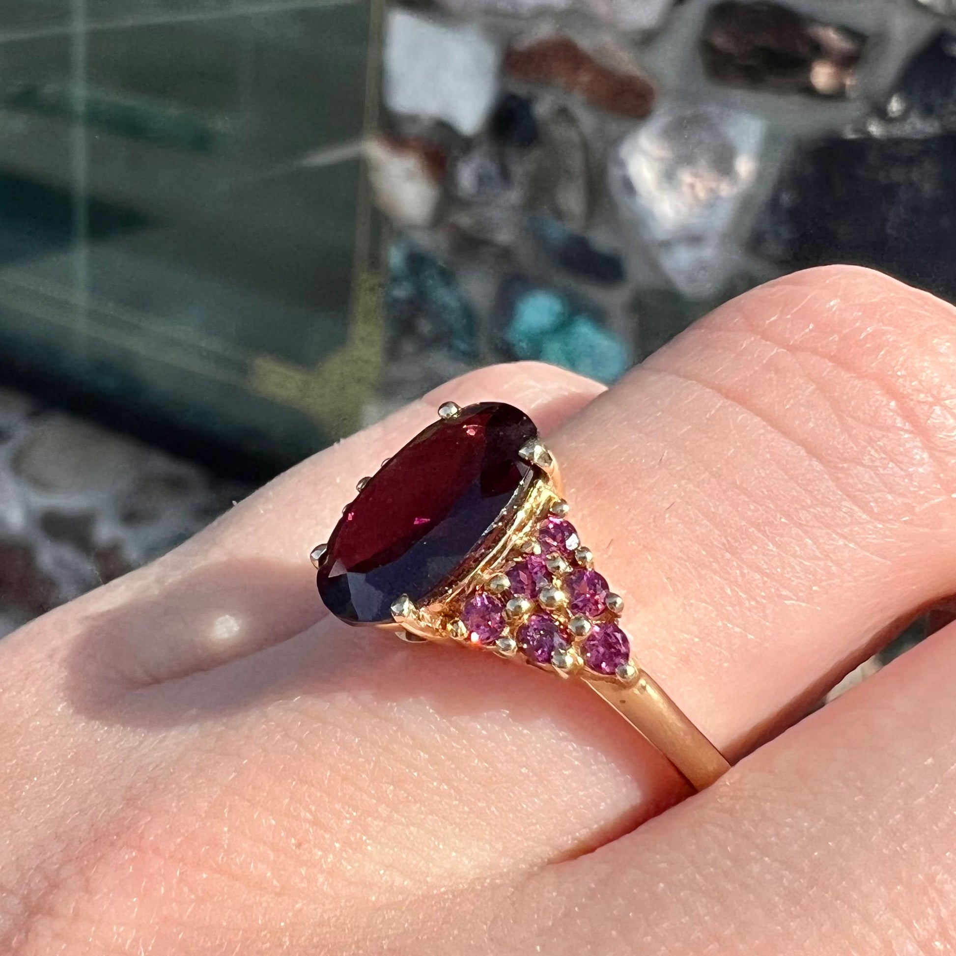 A ring with a crimson reddish purple stone set with clusters of round purple garnets on each side.