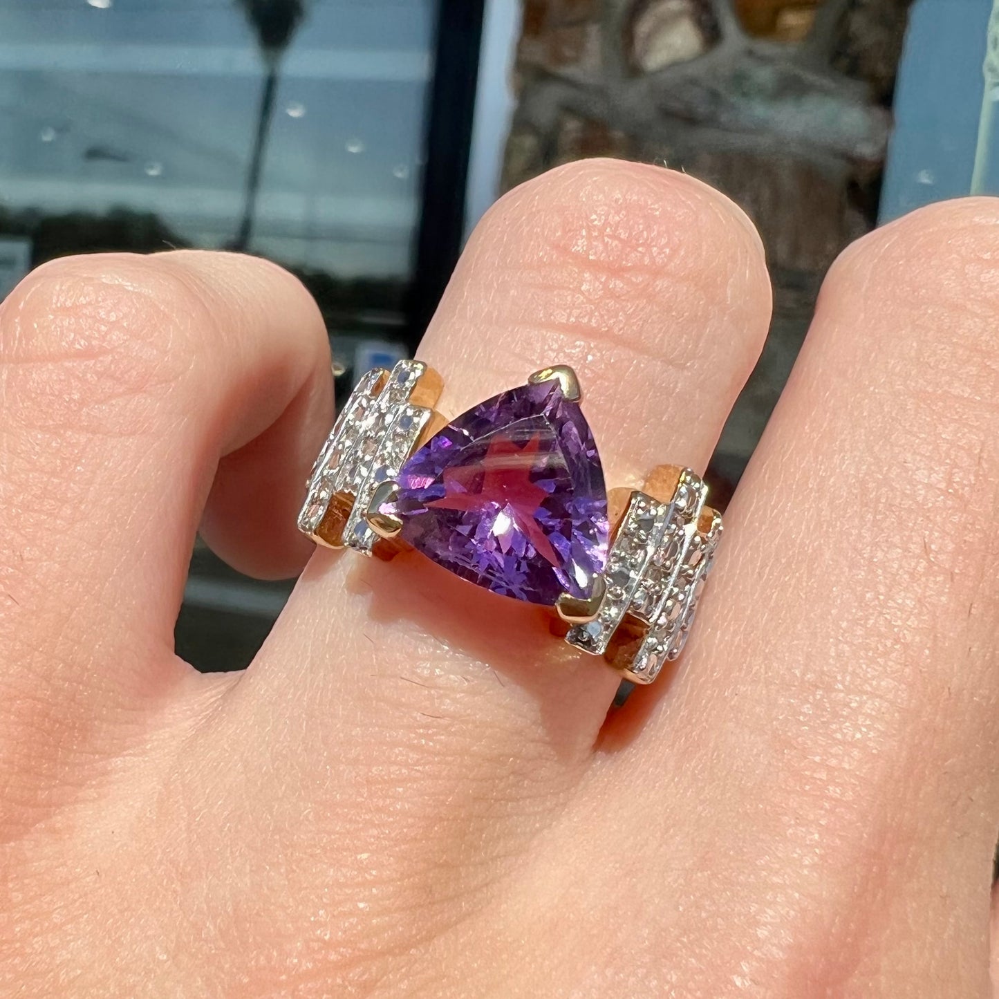 A yellow gold ring set with a trillion cut amethyst and round diamond accent stones.