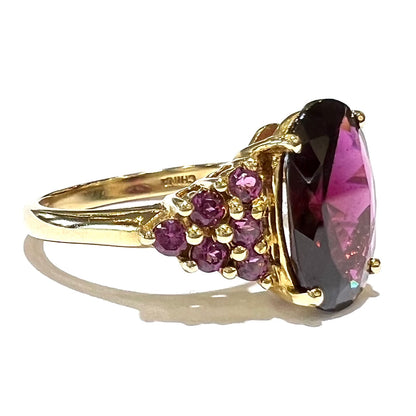 A yellow gold ring stamped "CHINA" set with clusters of purple garnets set on each side of a rhodolite garnet.