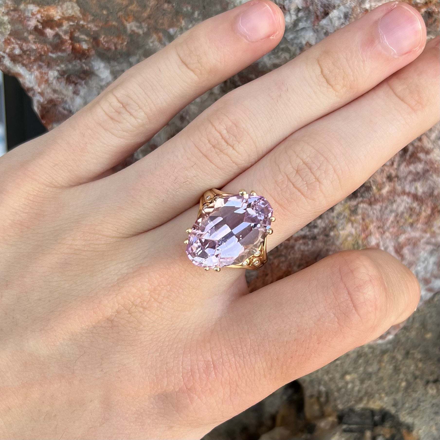 A large, pink kunzite is prong set into a 14kt yellow gold basket-style ring mounting with three diamonds flush set into the design on each side.