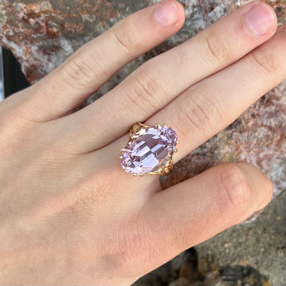 A large, pink kunzite is prong set into a 14kt yellow gold basket-style ring mounting with three diamonds flush set into the design on each side.