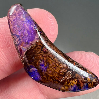 A loose boomerang shaped purple boulder opal stone from Quilpie, Australia.
