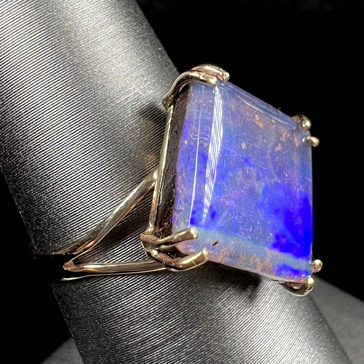 A ladies' boulder opal solitaire ring, handmade in yellow gold.  The stone is purple with flashes of blue, aqua, and green.