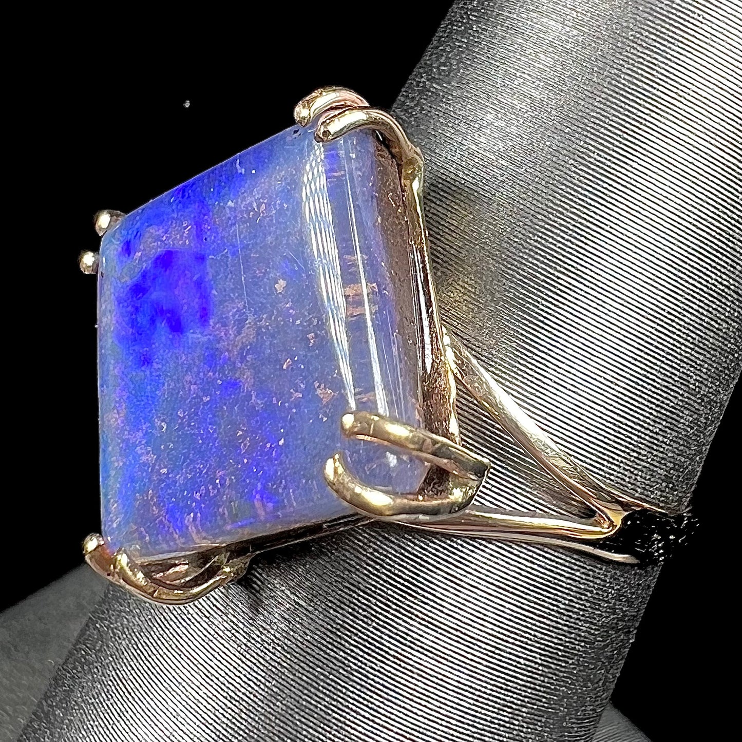 A ladies' boulder opal solitaire ring, handmade in yellow gold.  The stone is purple with flashes of blue, aqua, and green.