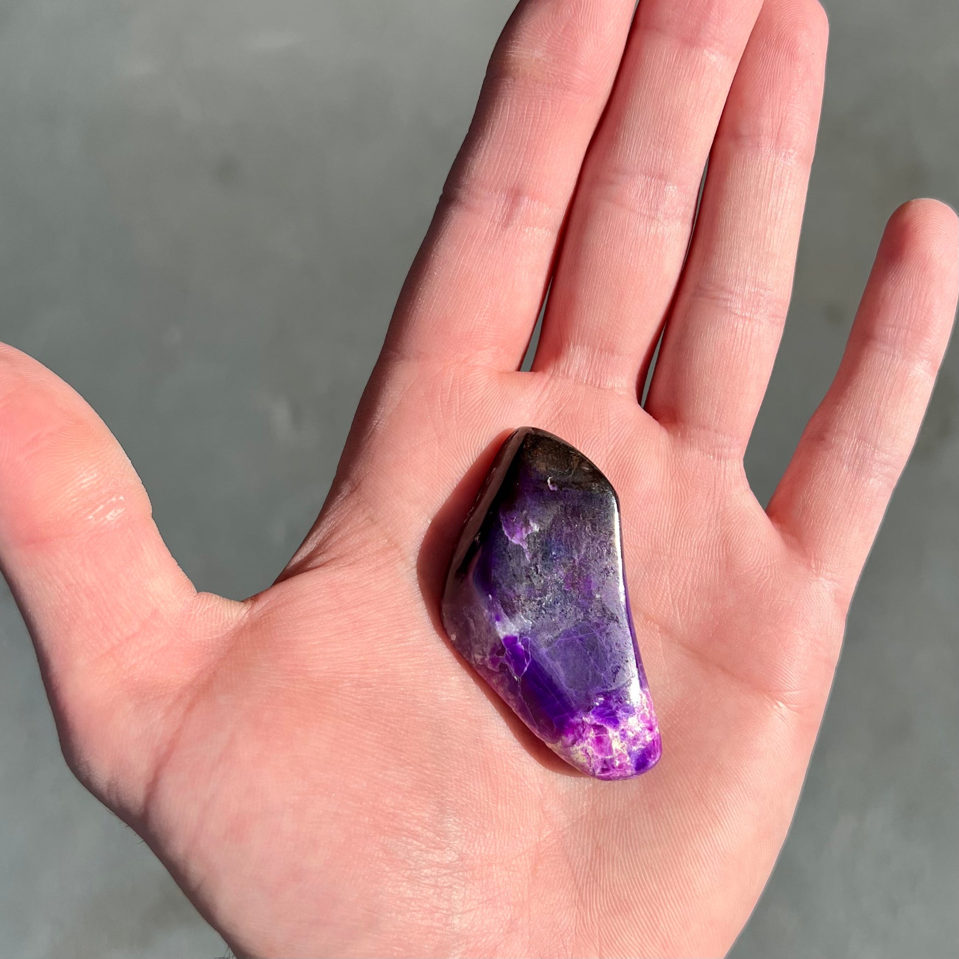 A loose, polished sugilite specimen displaying a blend of different shades of purple.