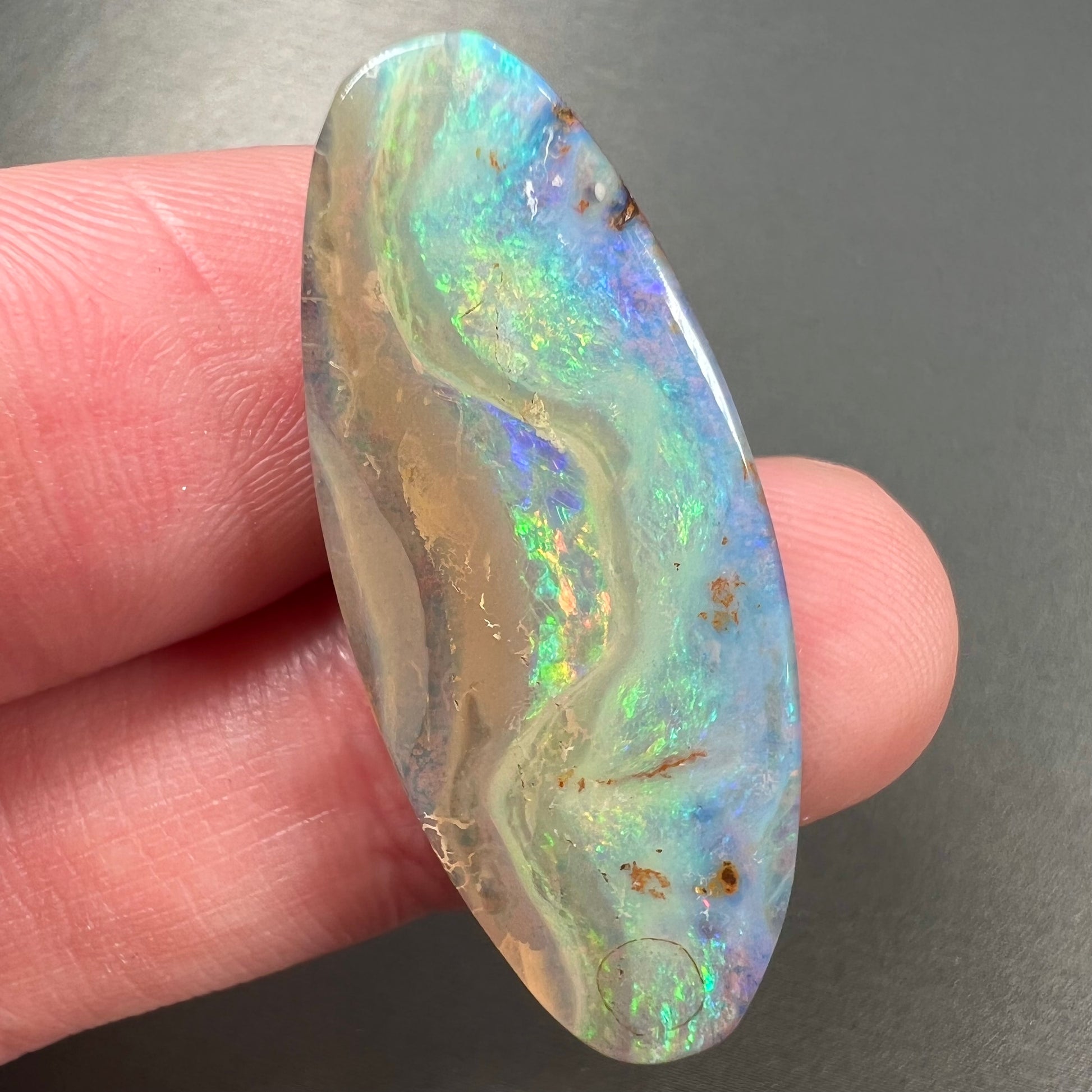 A loose, oval cabochon cut opal from Quilpie, Australia.  Blue, red, and green colors can be seen.