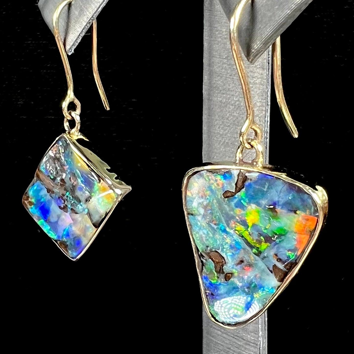 An asymmetric pair of French wire dangle yellow gold boulder opal earrings.  One opal is a square, and the other is a triangle.