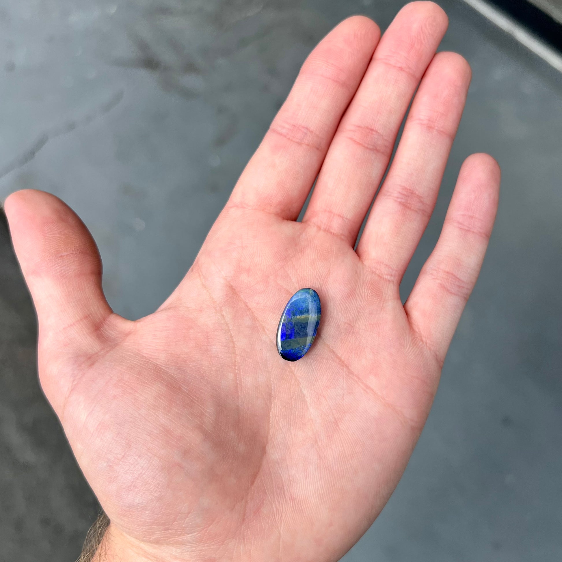 A loose, oval cabochon cut black boulder opal stone from Quilpie, Australia.