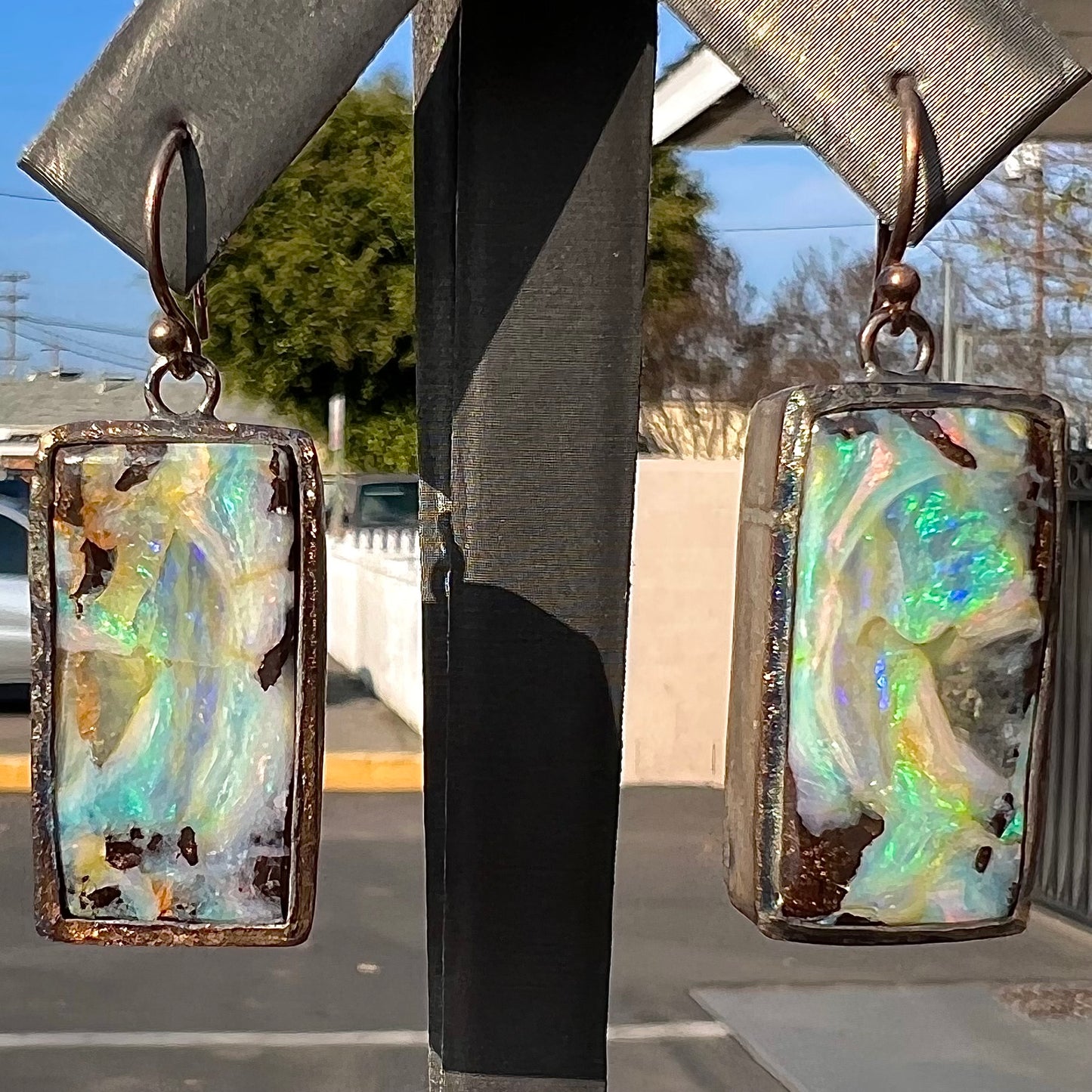 A pair of handmade sterling silver boulder opal earrings.  The earrings dangle from French wire hooks.