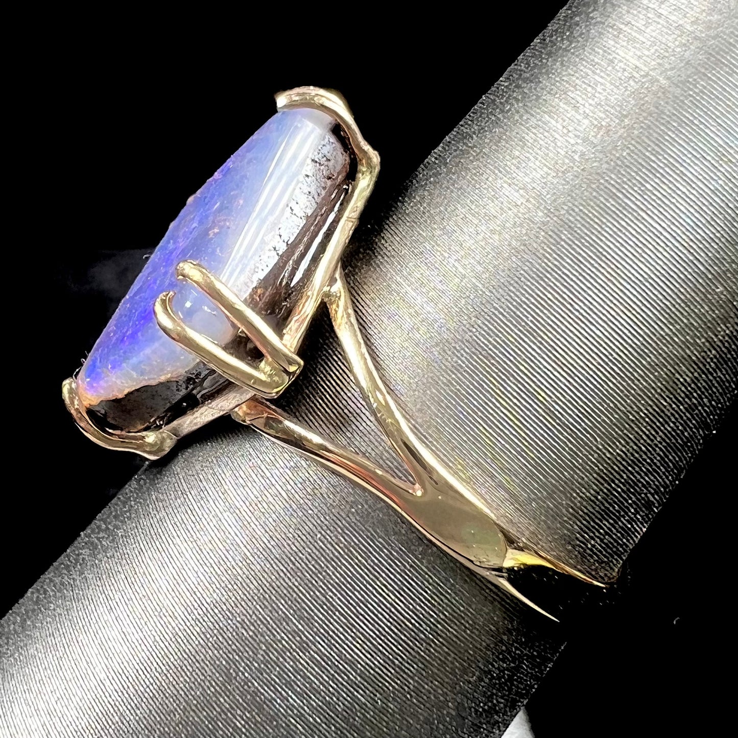 A ladies' boulder opal solitaire ring, handmade in yellow gold.  The stone is purple with flashes of blue, aqua, and green.