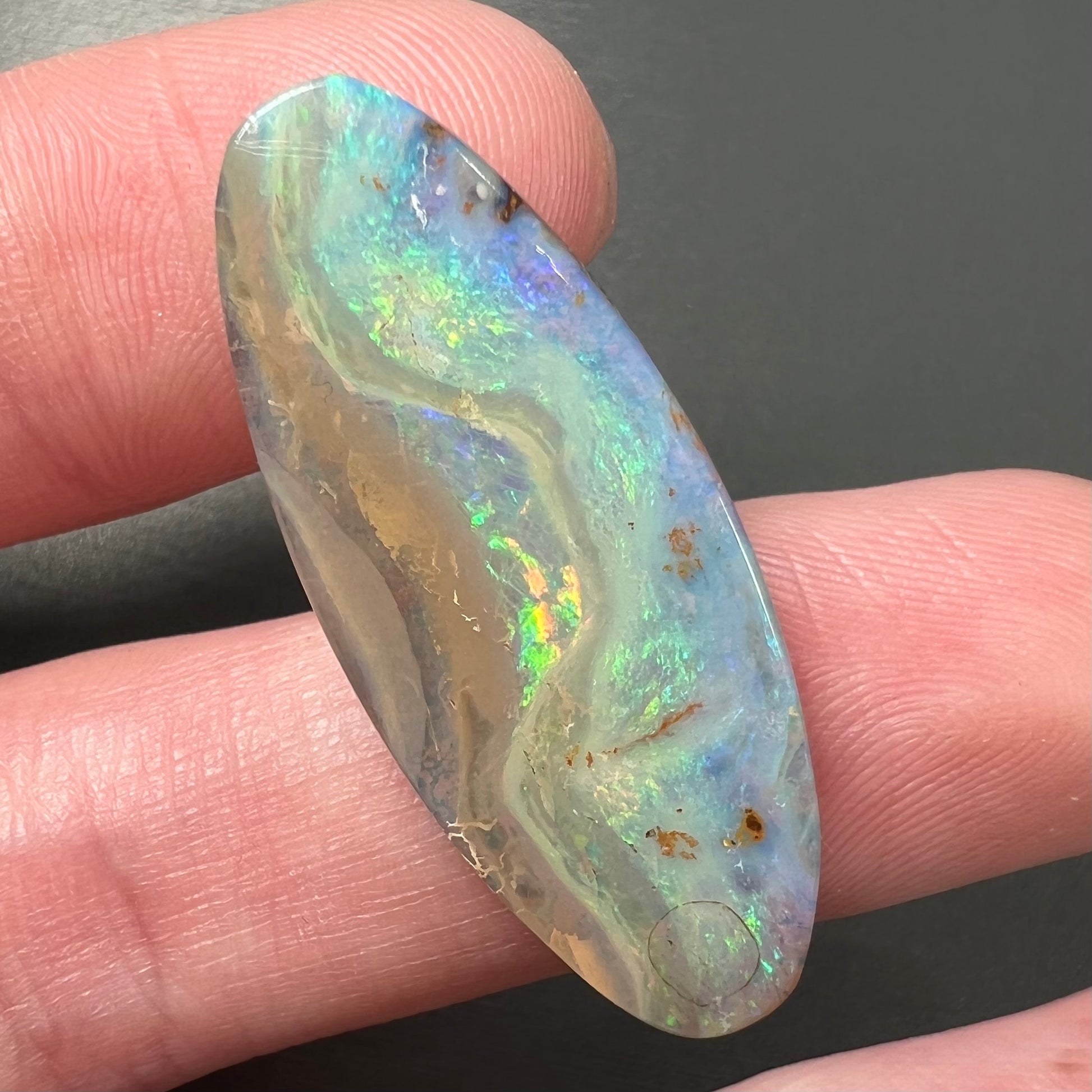 A loose, oval cabochon cut opal from Quilpie, Australia.  Blue, red, and green colors can be seen.