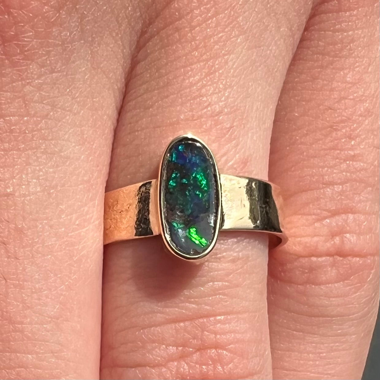 A blue green oval cabochon cut Australian boulder opal set in a yellow gold solitaire ring.