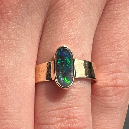 A blue green oval cabochon cut Australian boulder opal set in a yellow gold solitaire ring.