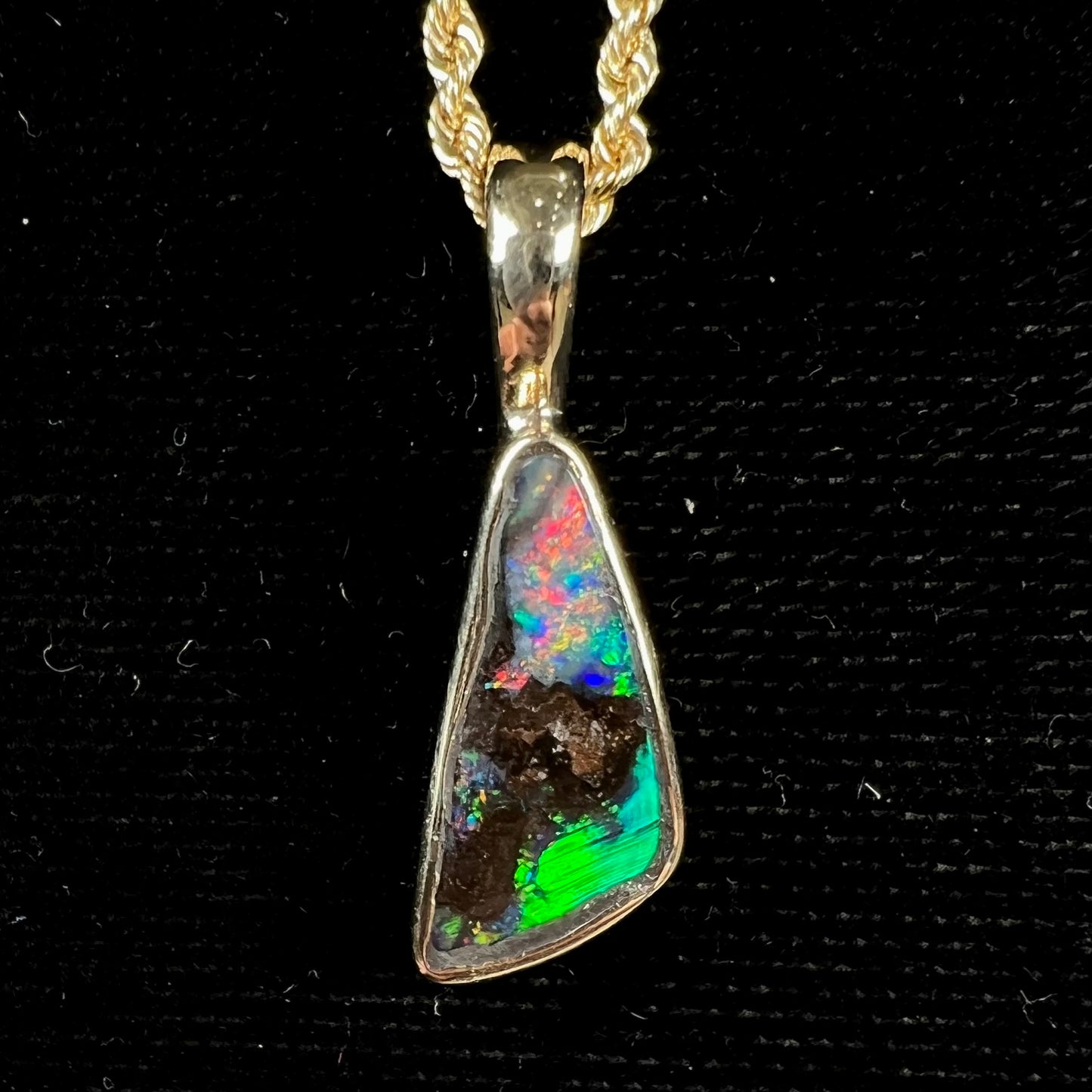 A bright green and red boulder opal bezel pendant in solid yellow gold.