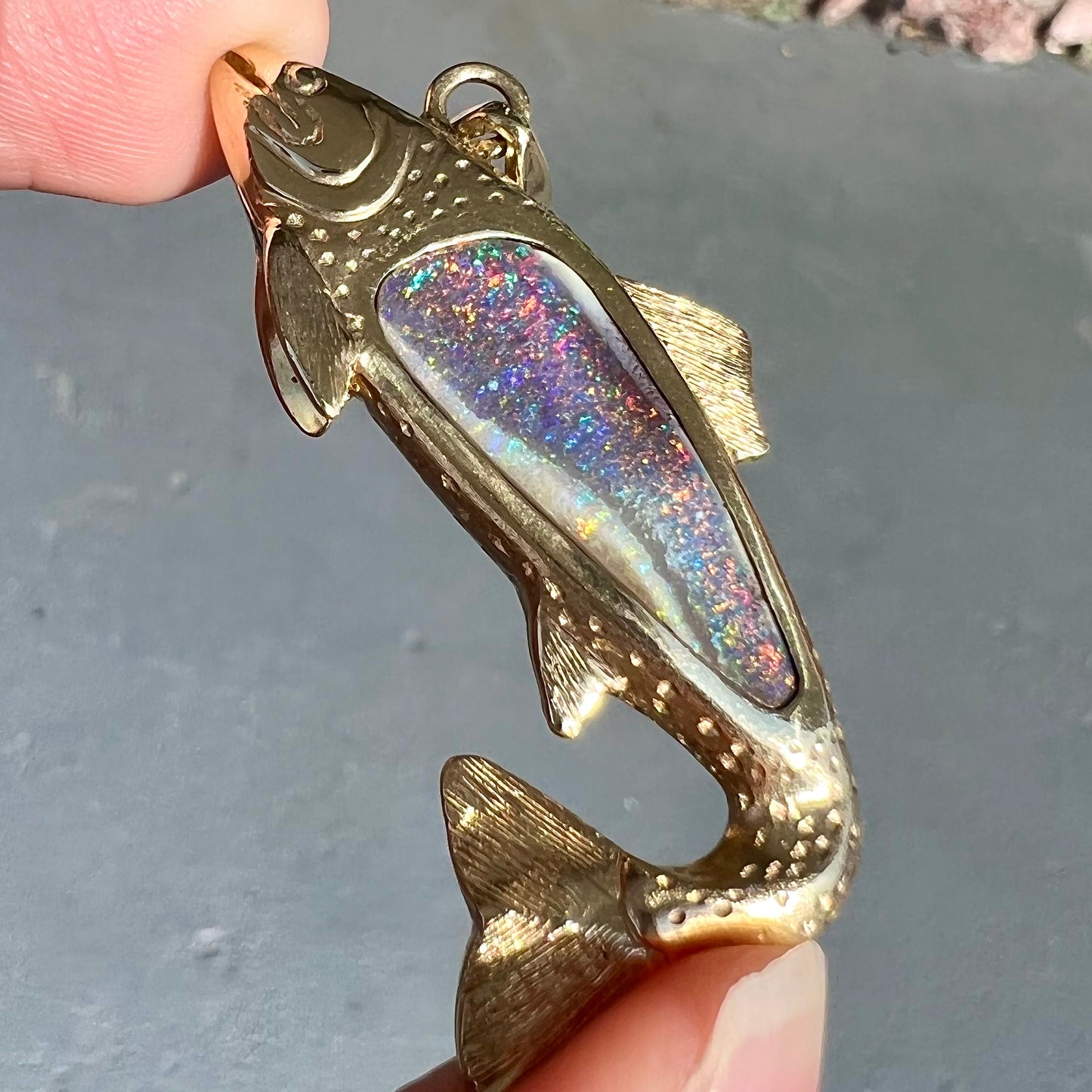 A yellow gold fish pendant detailed to look like a rainbow trout.  The body of the fish is set with a color changing black opal stone.