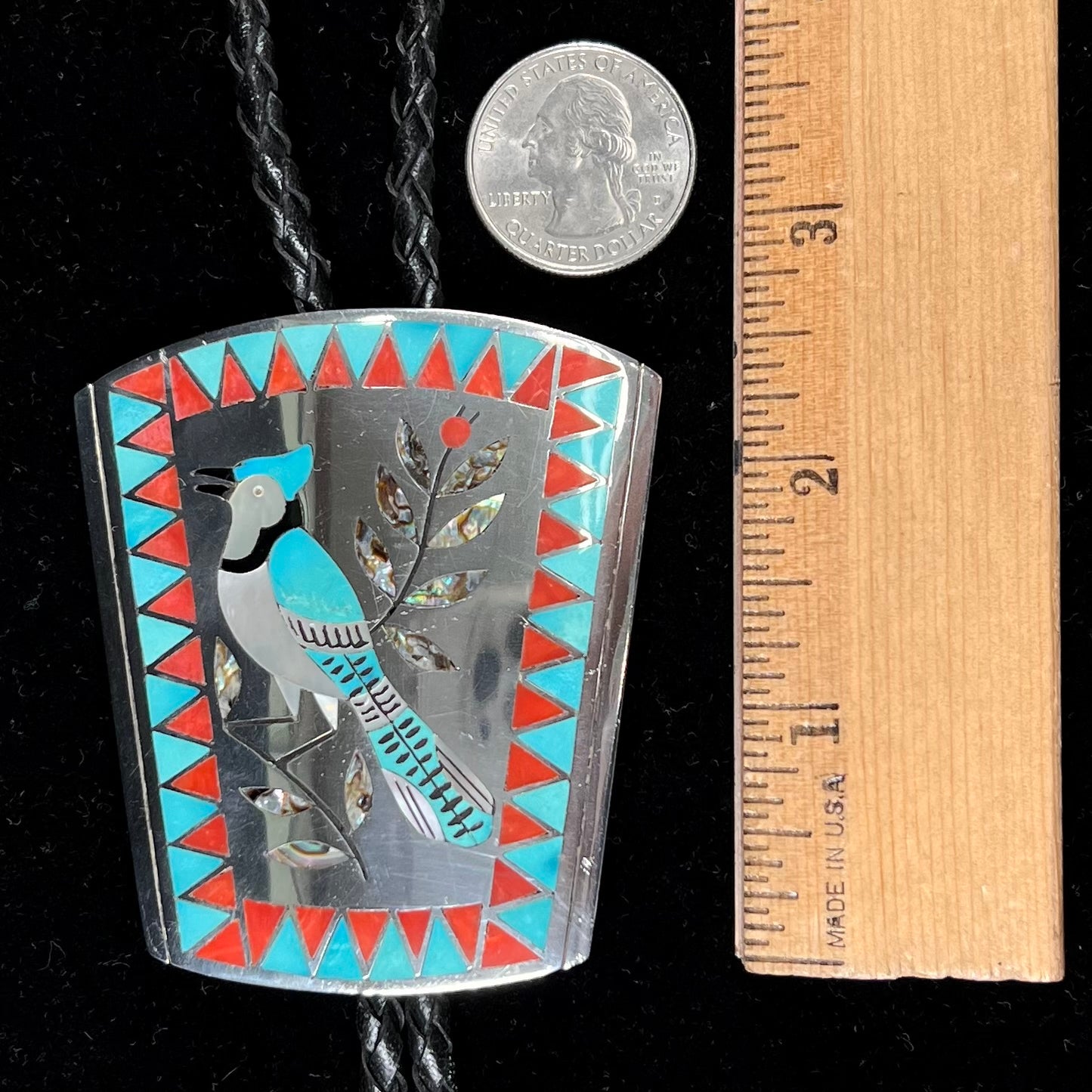 A turquoise and coral inlay bolo tie featuring the motif of a blue jay bird, handmade by Zuni artists Dennis and Nancy Edaakie.