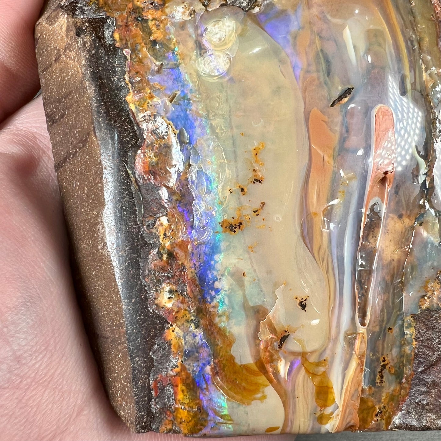 A polished Quilpie boulder opal specimen.  The stone has a stripe of bright blue, green, and purple.