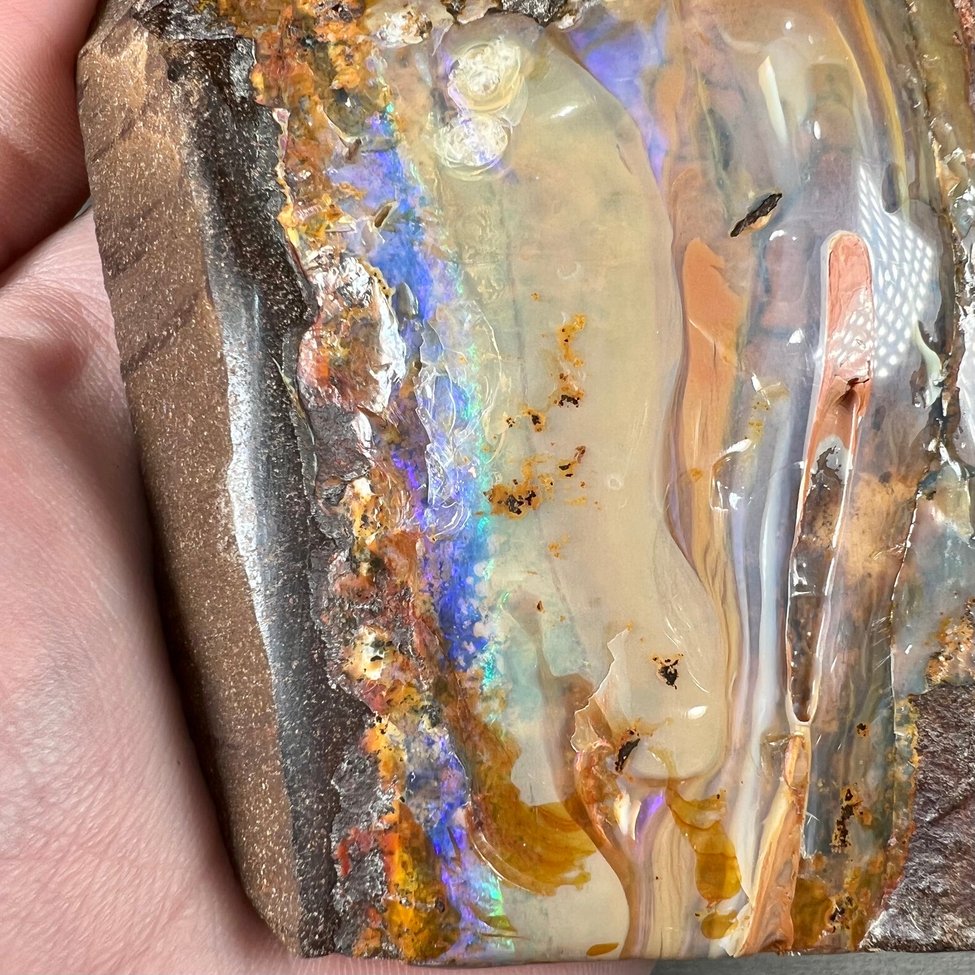 A polished Quilpie boulder opal specimen.  The stone has a stripe of bright blue, green, and purple.