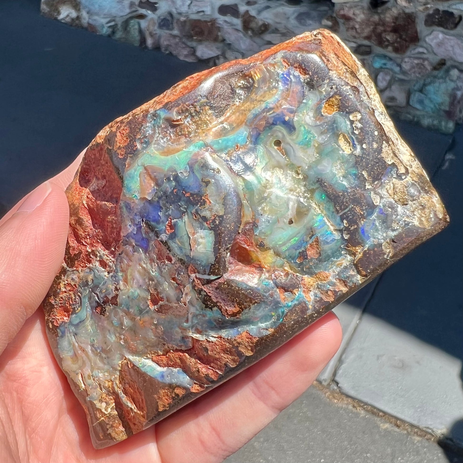 A hand-sized, polished Quilpie boulder opal specimen.  The stone shows blue, green, and orange flashes.
