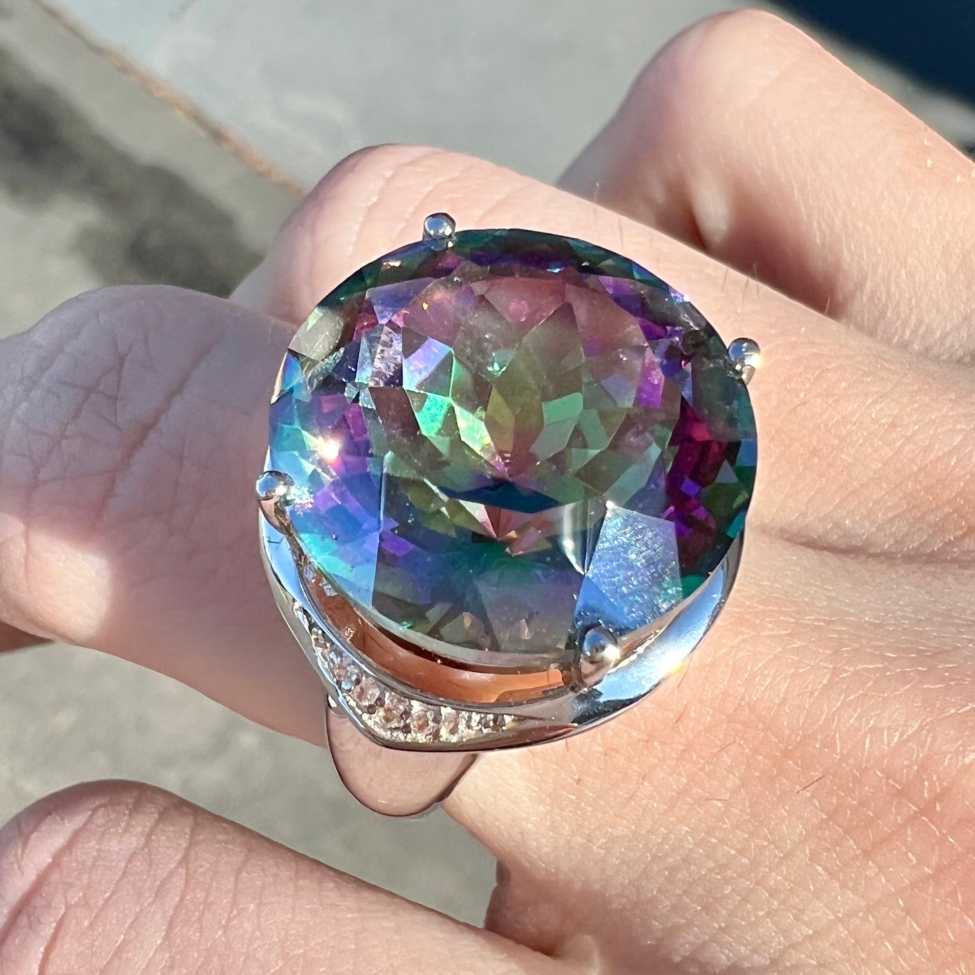 A large, round cut pink and green mystic topaz set in a sterling silver ring with white topaz accent stones.